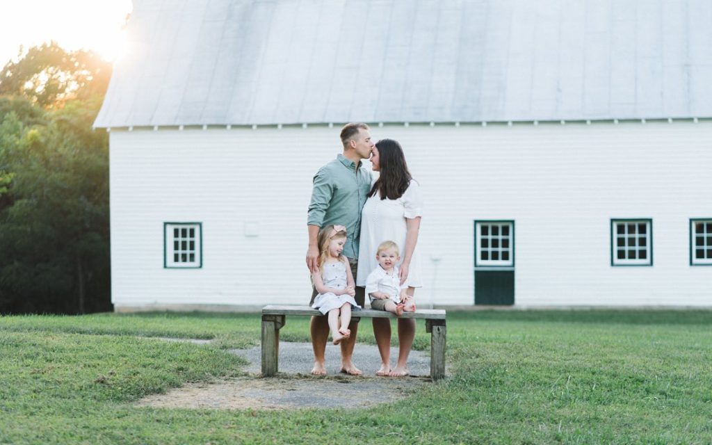 Family sitting together on bench with white barn | Family Photographers Dayton Ohio