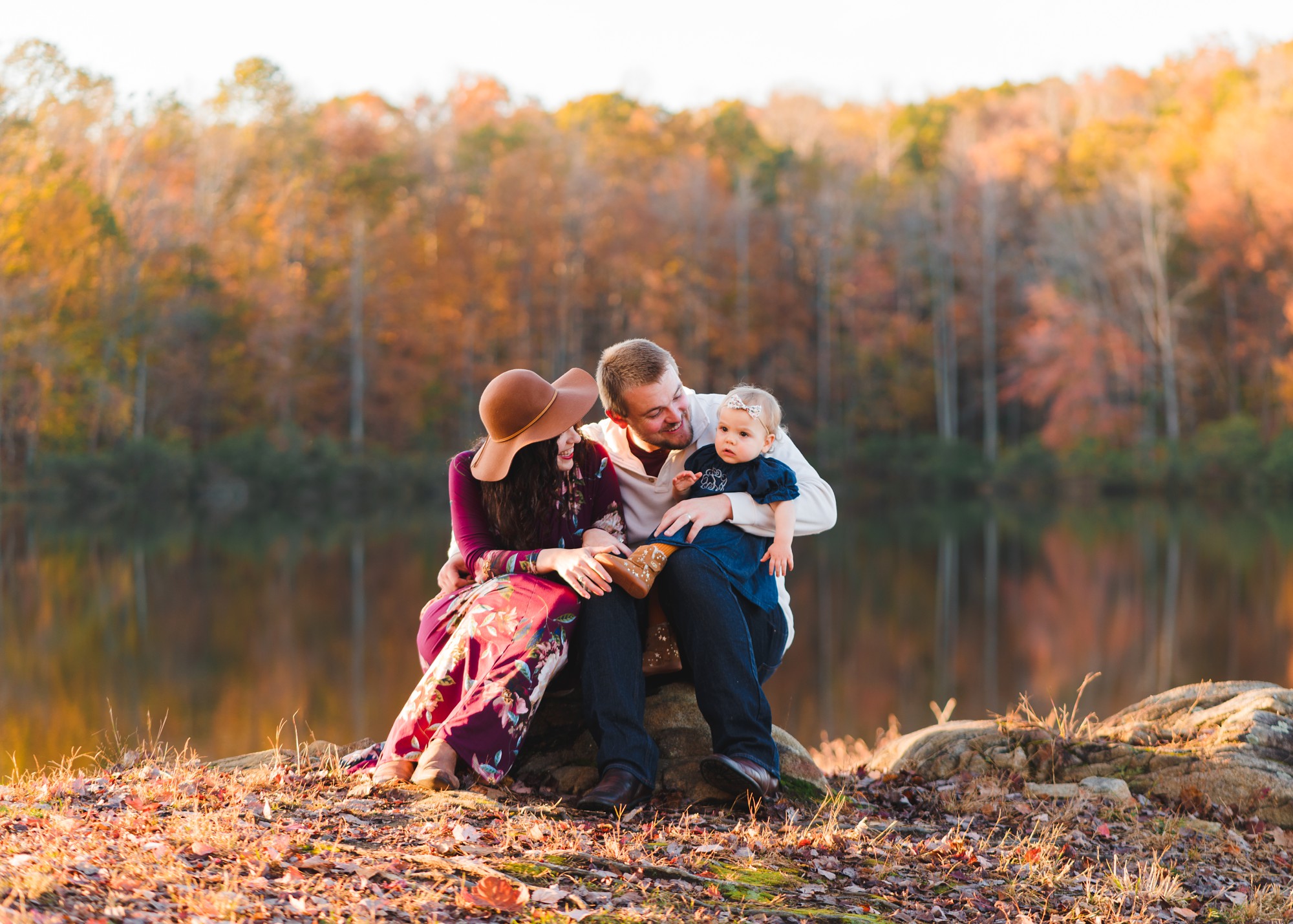 parents sitting on a rock with baby girl by a pond | Photographers in Charlottesville
