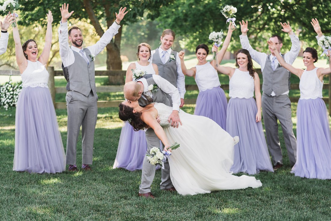 Groom dipping bride to kiss her with wedding party near them | Running Mare Farm Wedding