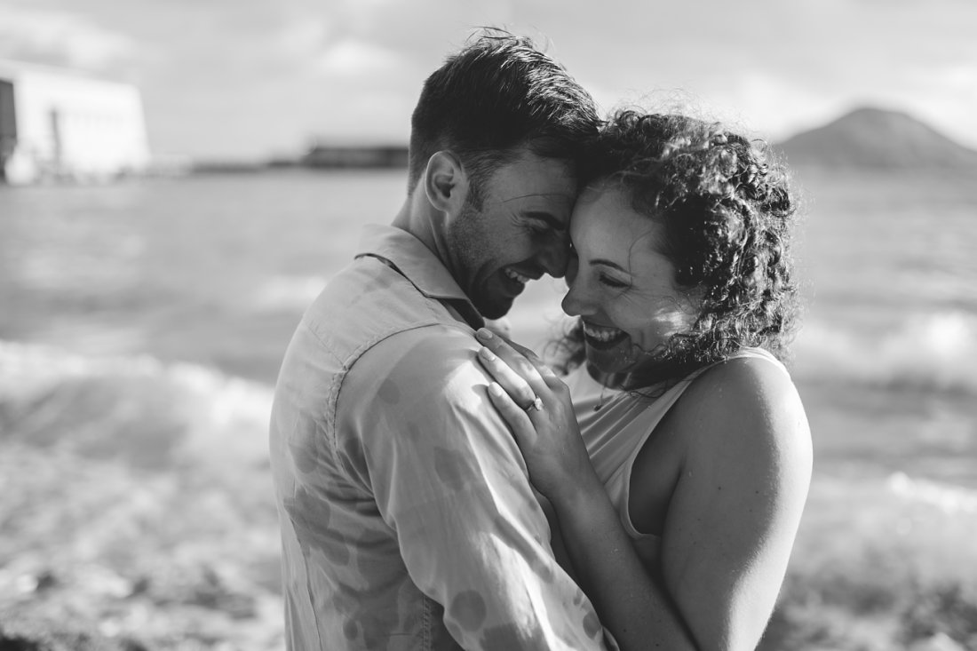 man and woman laughing with beach behind them | beach engagement photos