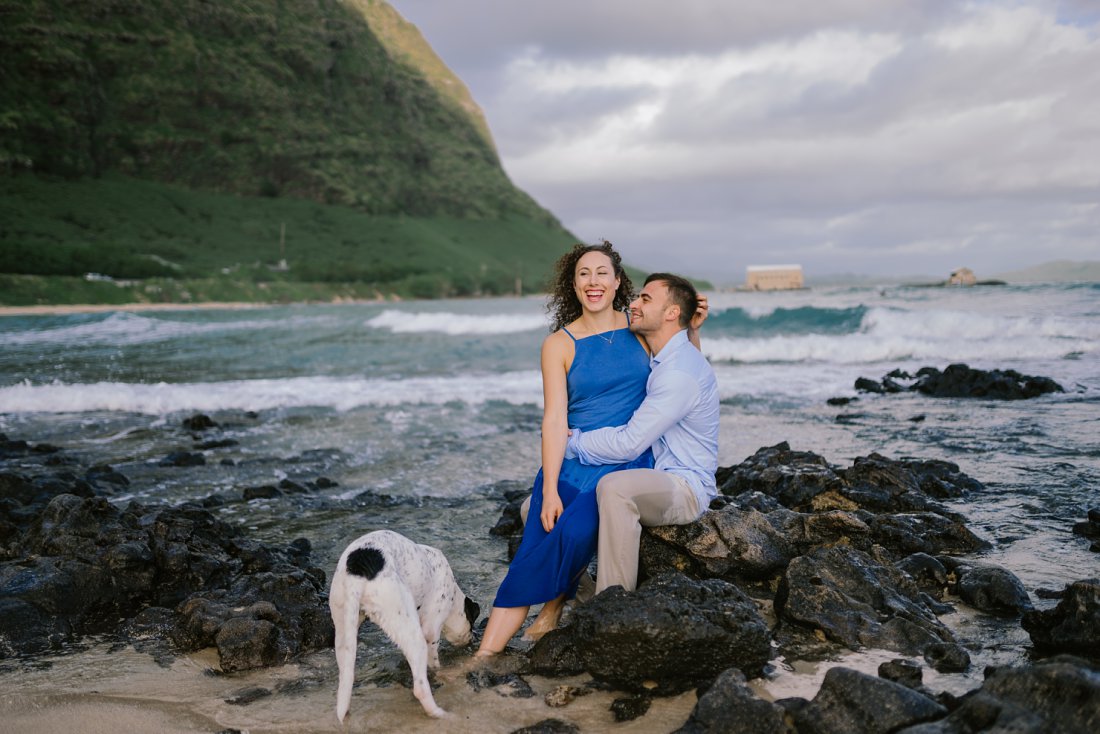 couple sitting on rocks on beach with dog | beach engagement photos
