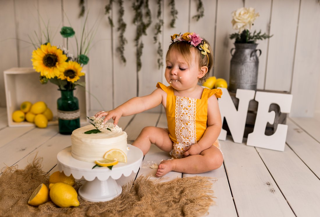 baby girl in yellow outfit touching cake | Dayton First Birthday Photographer