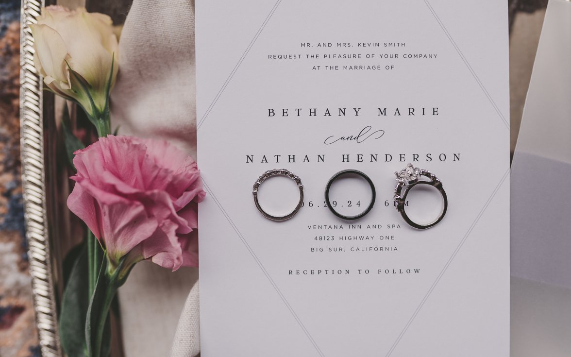 wedding invitation with rings on top of it next to flower