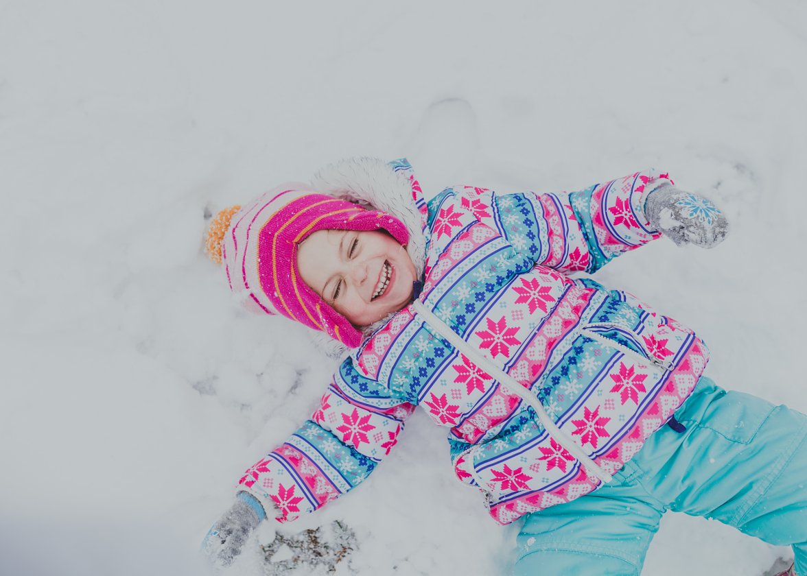 little girl smiling laying down in the snow in colorful clothes