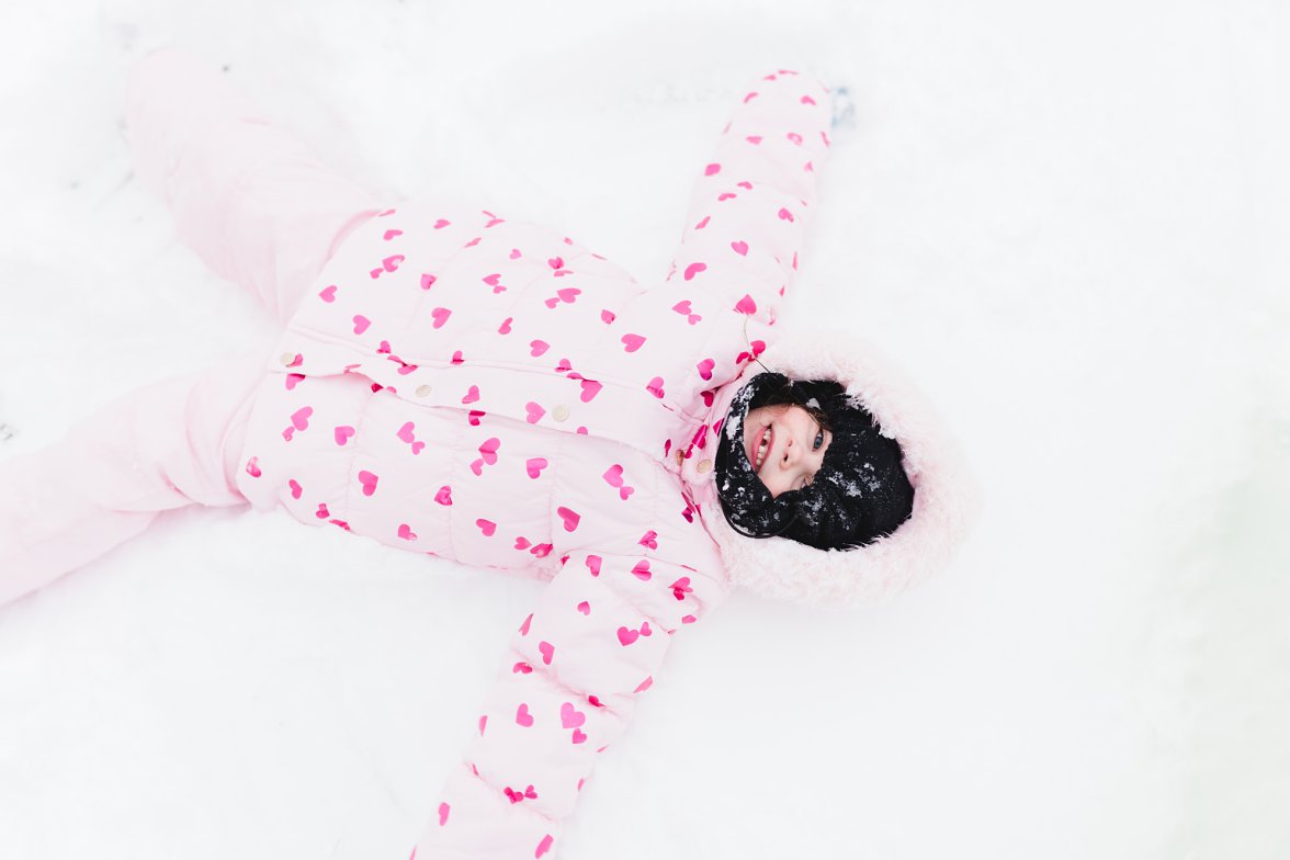 little girl in pink jacket laying in snow