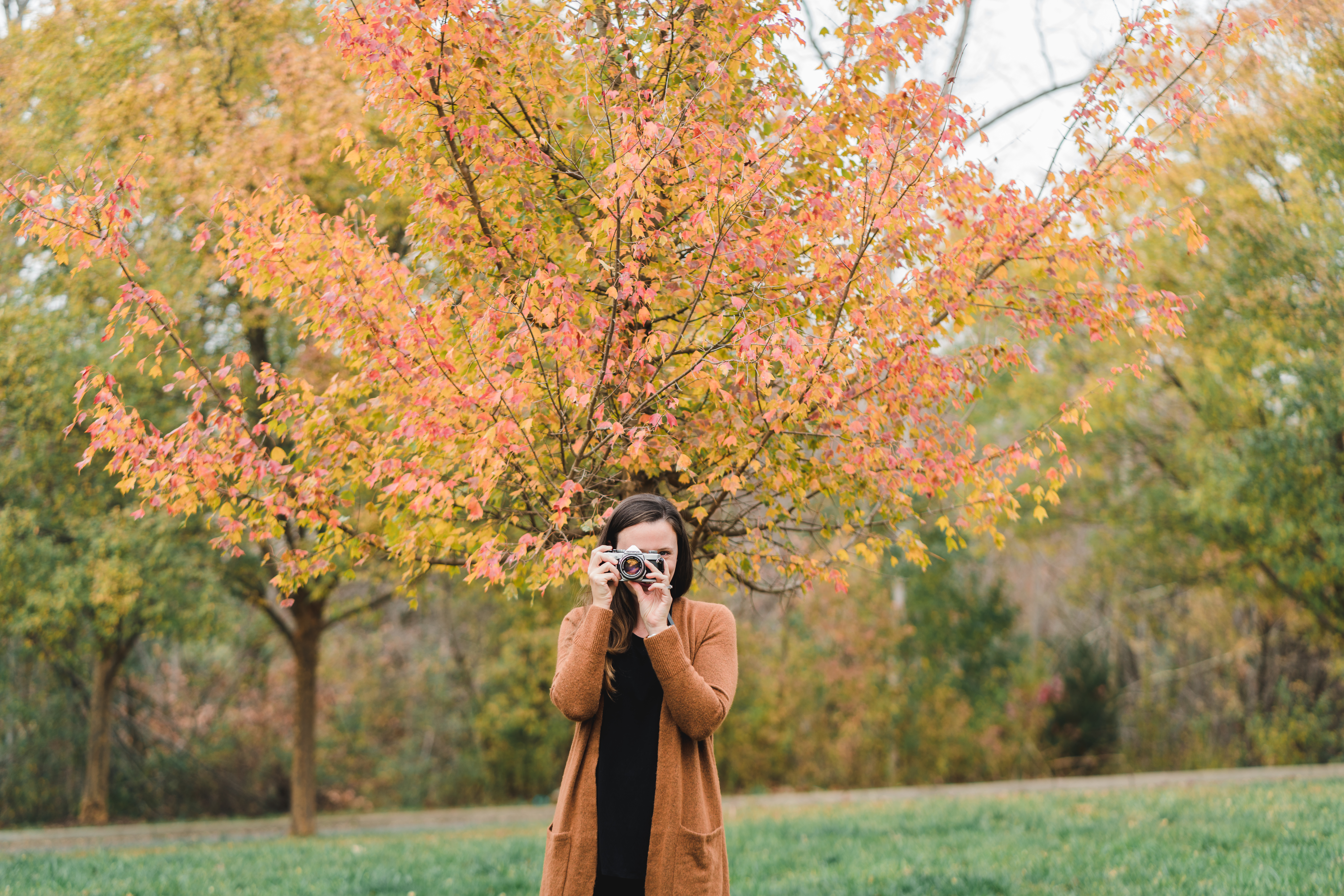 woman holding old camera up to her eye with orange tree behind her
