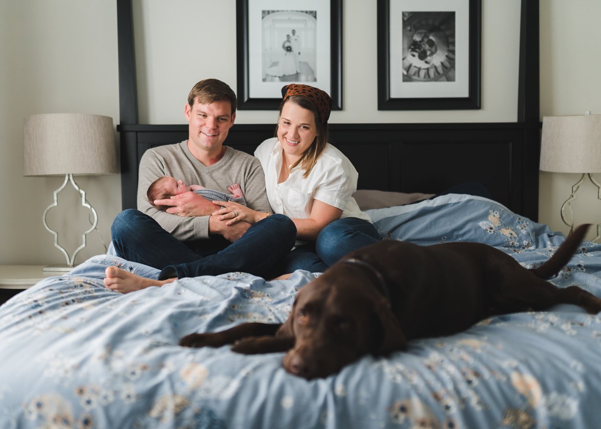Family of three sitting on bed with their dog 