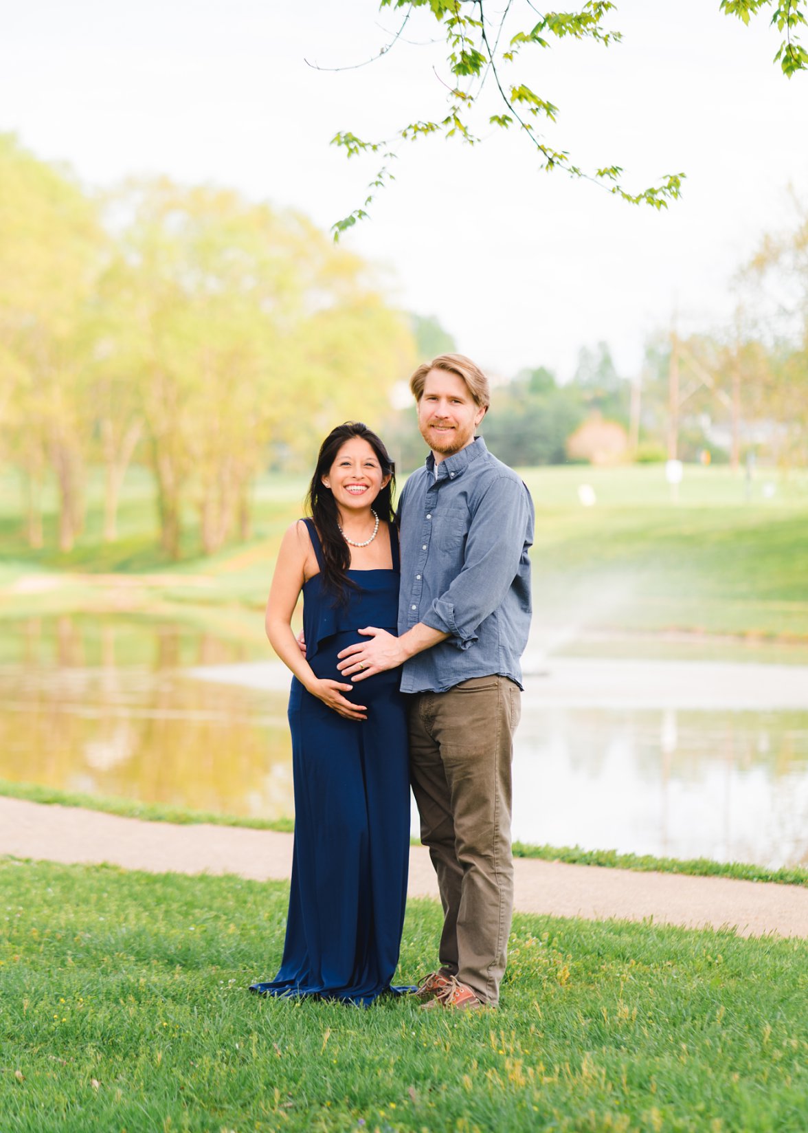 couple holding baby belly in front of pond 