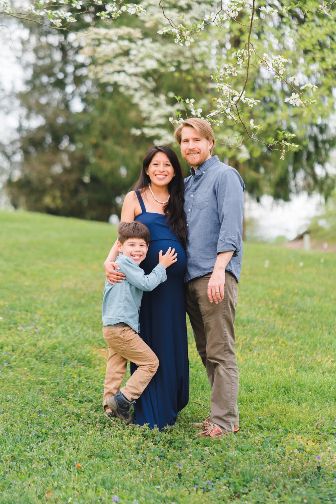 family of three standing in grass with tree blooms | Montgomery, Alabama Maternity Photographer